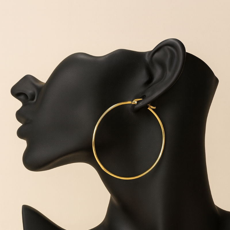 Gold hoop earring on a black mannequin ear with a beige background