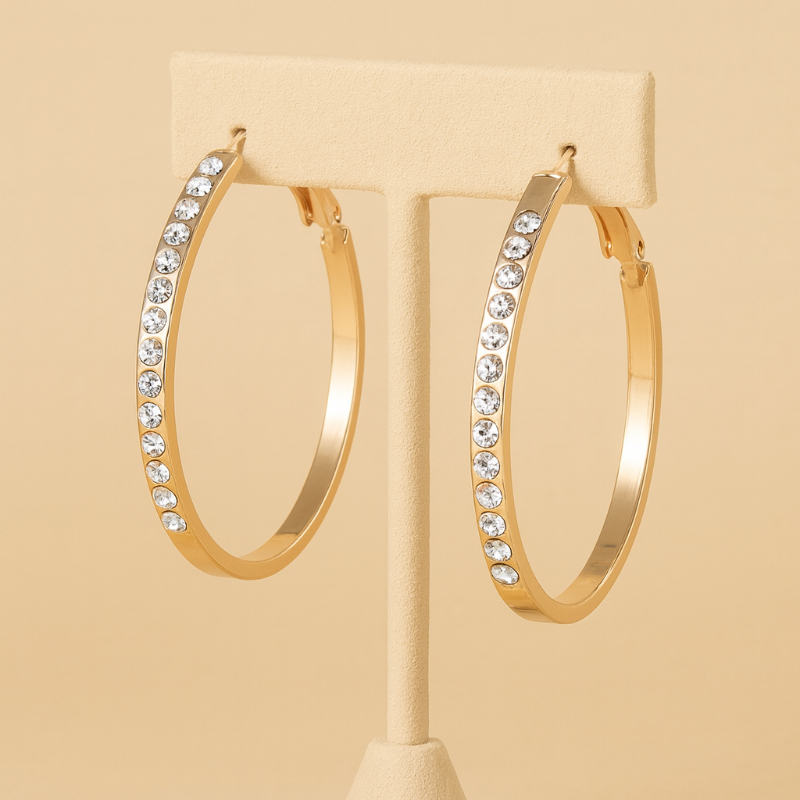 Gold hoop earrings with crystal accents on a beige stand against a beige background