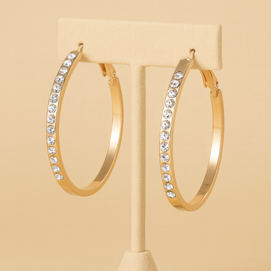 Gold hoop earrings with crystal accents on a beige stand against a beige background