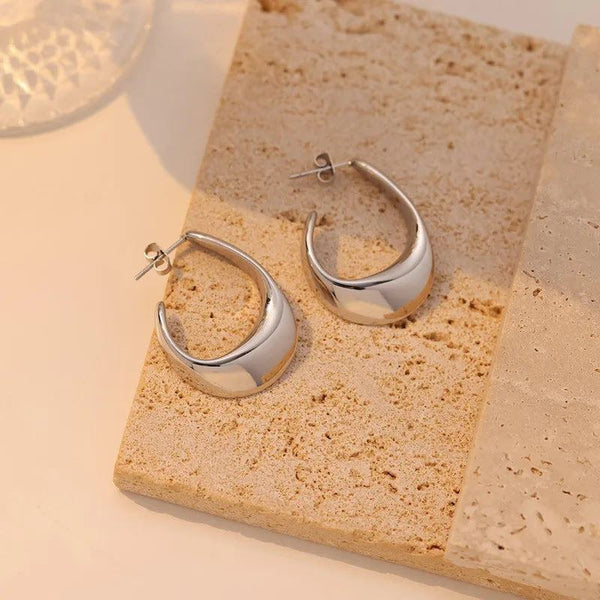 Stainless steel white gold plated ear studs on textured surface.