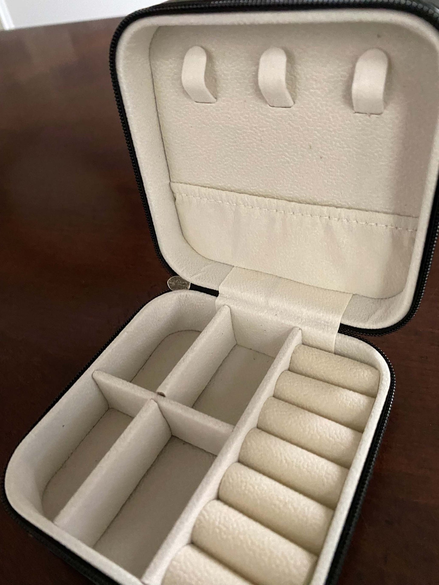 Open beige jewelry case with compartments on a wooden surface