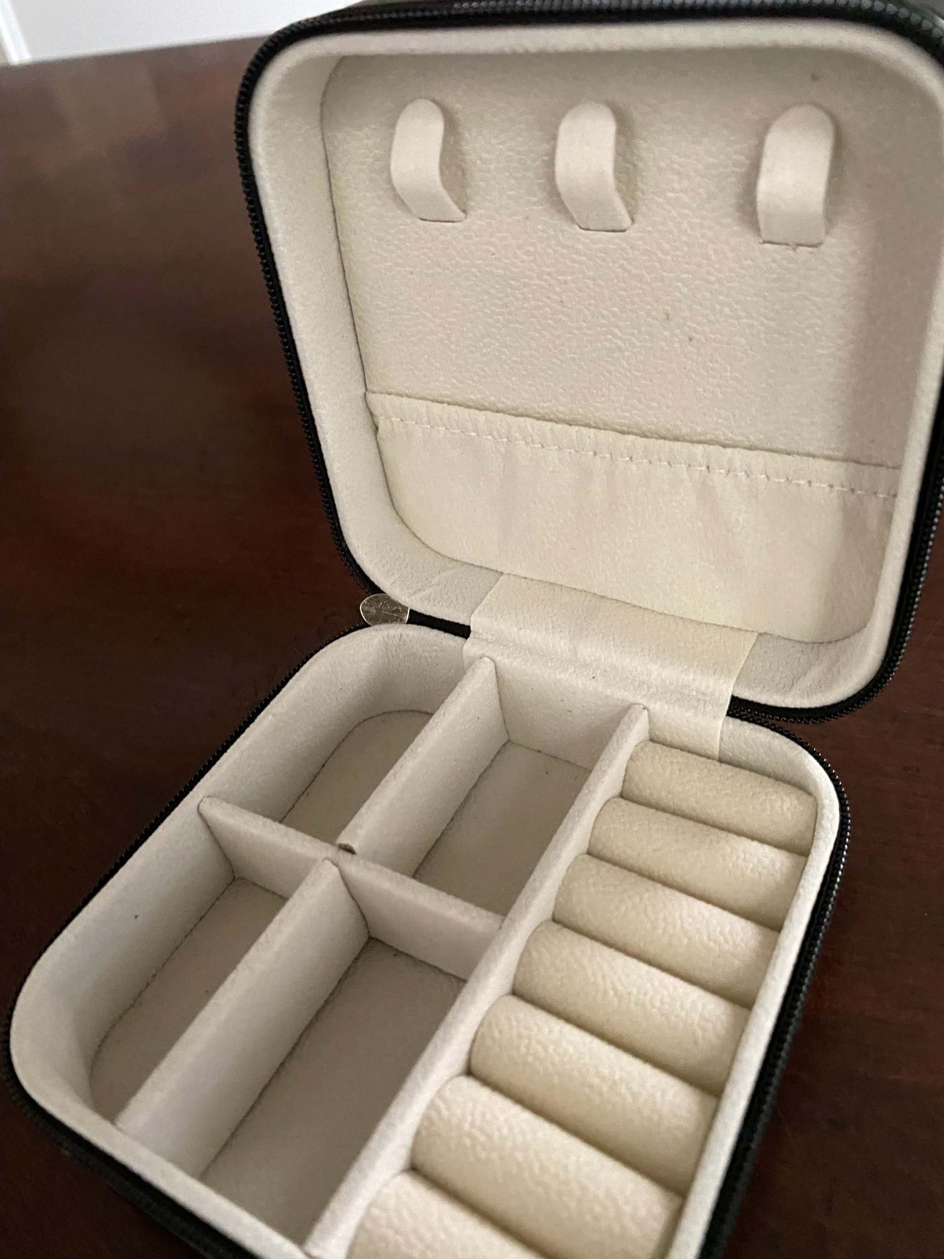 Open beige jewelry case with compartments on a wooden surface