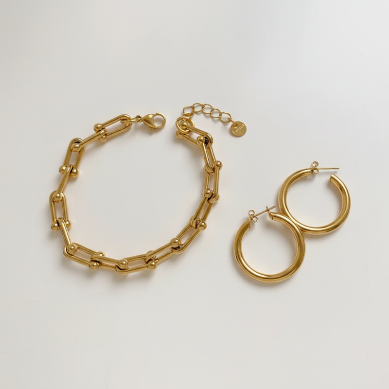 The Gold Everyday Essentials gold link bracelet and chunky hoop earrings set on white background